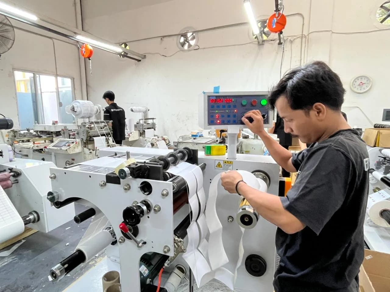 A factory technician adjusting the controls of a label converting machine on the production floor